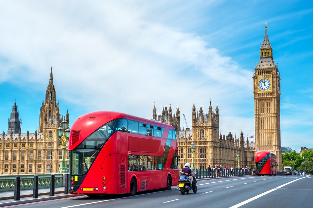 Red double-decker buses pass by Big Ben, London