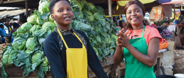 Two happy African female traders standing together in front of their stall in a market