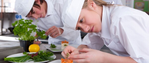 Two young trainee chefs garnishing desert in a kitchen